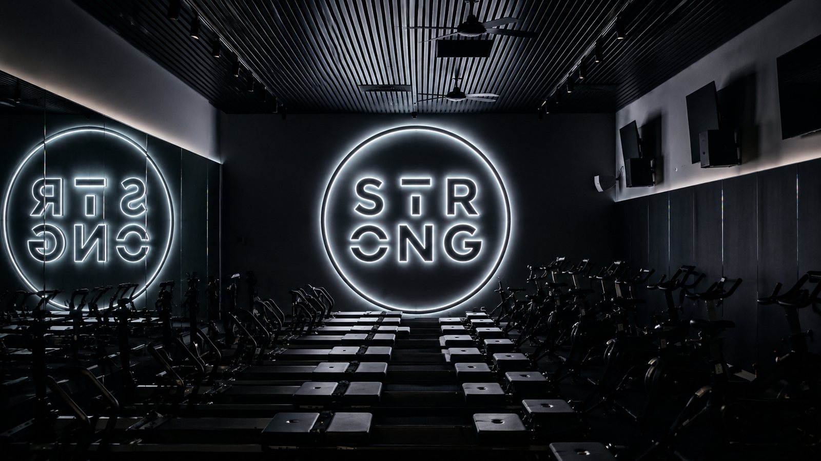 Circular LED-lit logo sign on the end wall of a reformer fitness studio